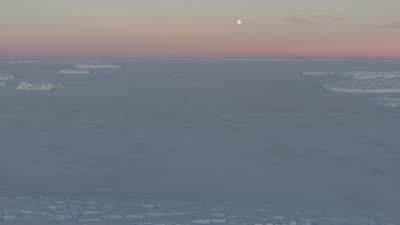 Survol des terres glacées sous un ciel rosé et le soleil bas de l'été austral