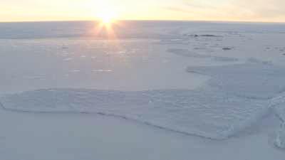 Survol des terres glacées sous un ciel rosé et le soleil rasant de l'été austral