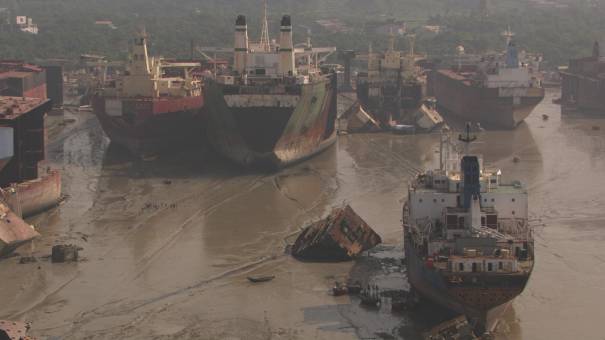 Carcasses de bateaux démantelés en bord de mer, ouvriers au travail